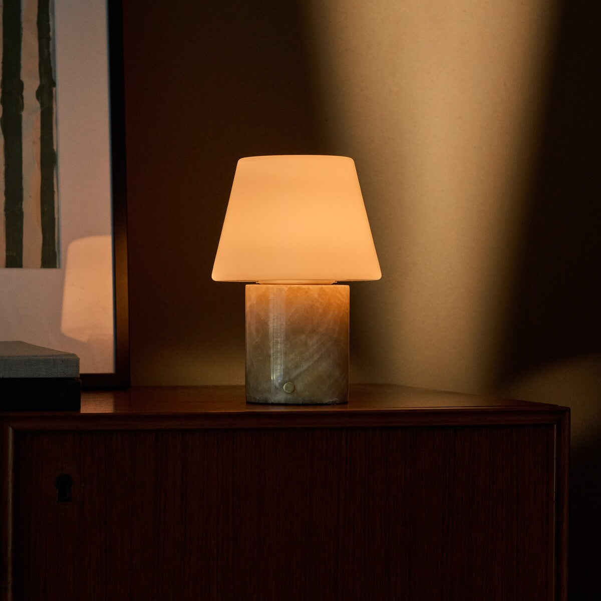 Oplaadbare tafellamp Hooch in Honey Onyx marmer op een walnoten kast tegen een olijfgroene wand
