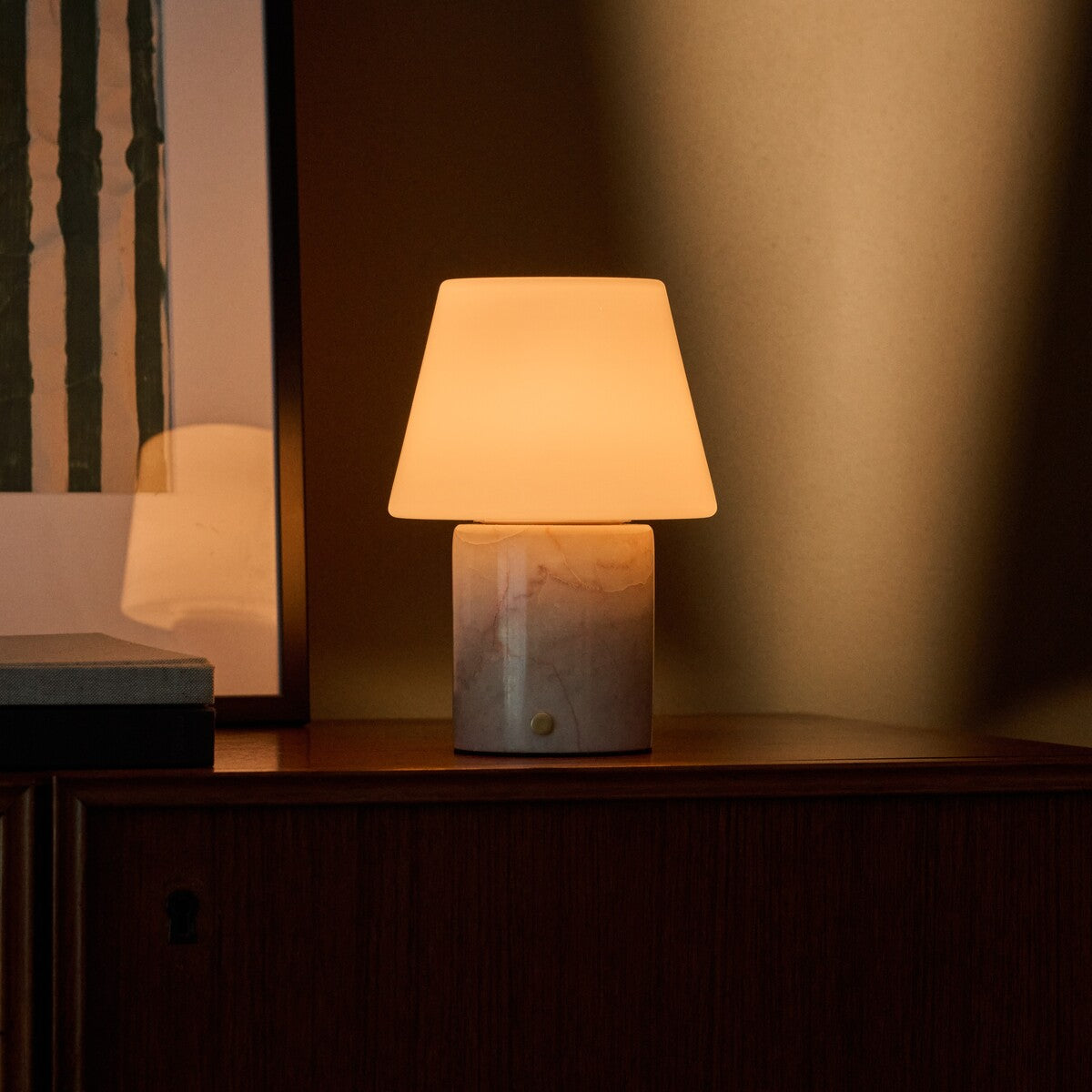 Oplaadbare tafellamp Hooch in Rosa Aurora marmer op een donker houten dressoir in avondlicht