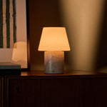 Oplaadbare tafellamp Hooch in Rosa Aurora marmer op een donker houten dressoir in avondlicht