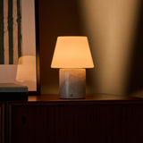 Oplaadbare tafellamp Hooch in Rosa Aurora marmer op een donker houten dressoir in avondlicht