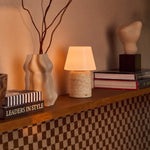 Tafellamp oplaadbaar Hooch Large in beige travertin op een houten plank naast boeken en een keramische vaas