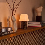 Tafellamp oplaadbaar Hooch Large Emperador Dark Marble op een plank naast een keramische vaas en boeken