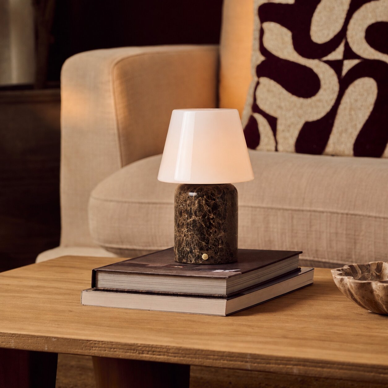 Tafellamp oplaadbaar Hooch Large Emperador Dark Marble op een stapel boeken naast een beige fauteuil