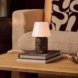 Tafellamp oplaadbaar Hooch Large Emperador Dark Marble op een stapel boeken naast een beige fauteuil