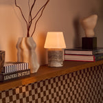 Tafellamp oplaadbaar Hooch Large in silver travertine op een houten plank naast boeken en een keramische vaas