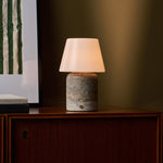 Oplaadbare tafellamp Hooch Large in silver travertine verlicht een donker houten dressoir tegen een olijfgroene muur