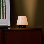 Oplaadbare tafellamp Hooch Small Nero Marquina Marble brandend op een houten kast naast gestreepte wandkunst