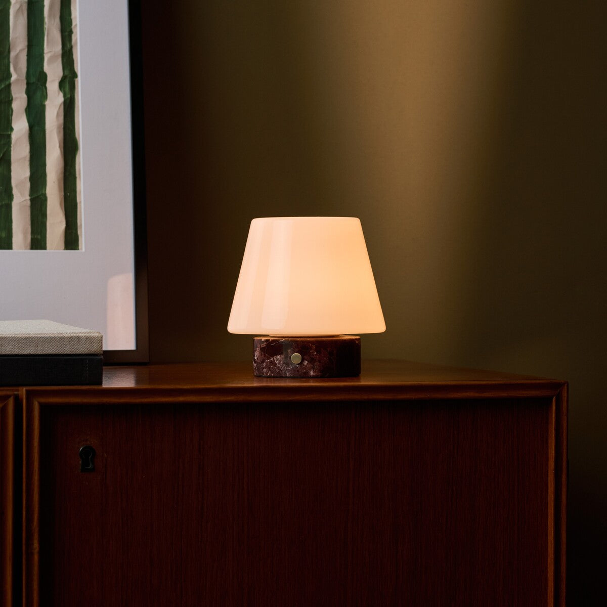 Tafellamp oplaadbaar Hooch Small Rosso Levanto Marble brandend op een donkere kast naast gestreepte kunst