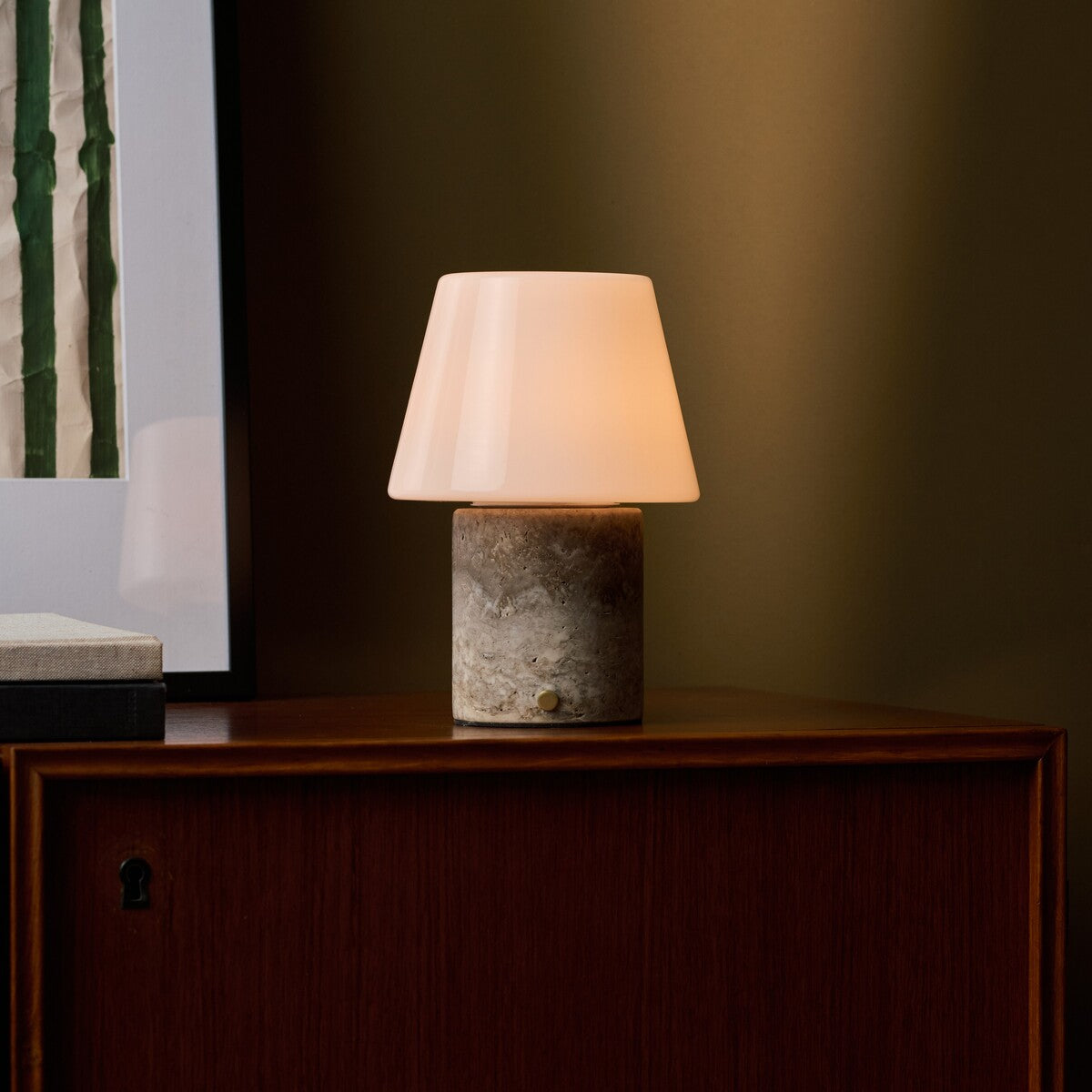 Oplaadbare tafellamp Hooch in Silver Travertine, brandend op een houten kastje bij groene muur