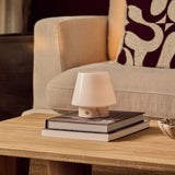 Tafellamp oplaadbaar Hooch Small in Rosa Aurora marmer op gestapelde boeken naast een beige fauteuil