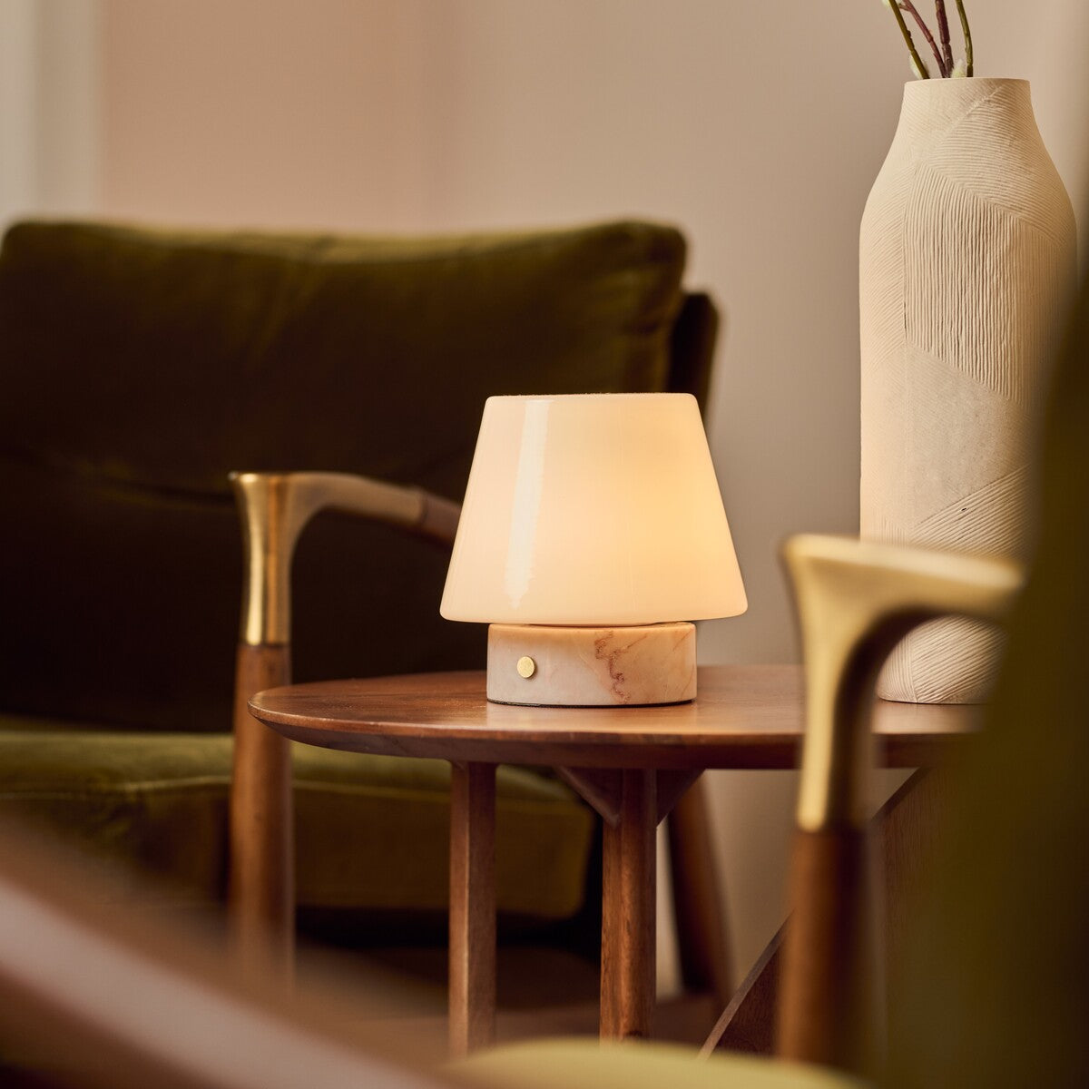 Tafellamp oplaadbaar Hooch Small in Rosa Aurora marmer op een houten bijzettafel tussen olijfgroene fauteuils