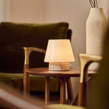 Tafellamp oplaadbaar Hooch Small in Rosa Aurora marmer op een houten bijzettafel tussen olijfgroene fauteuils