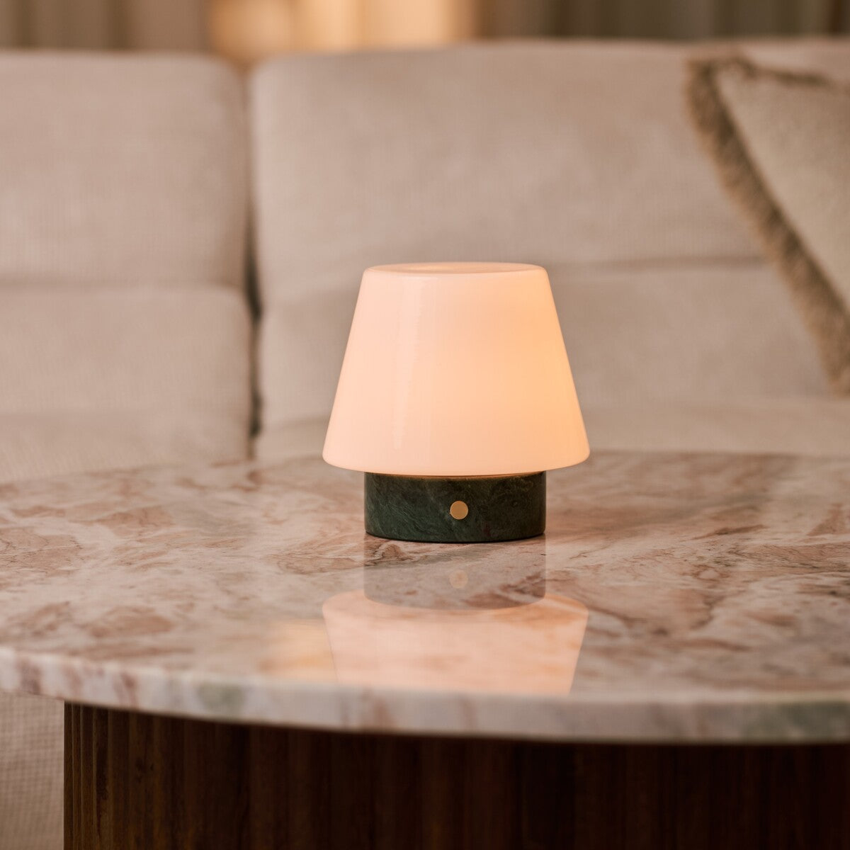 Tafellamp oplaadbaar Hooch Small Verde Alpi Marble brandend op een ronde marmeren salontafel naast een bank