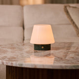 Tafellamp oplaadbaar Hooch Small Verde Alpi Marble brandend op een ronde marmeren salontafel naast een bank