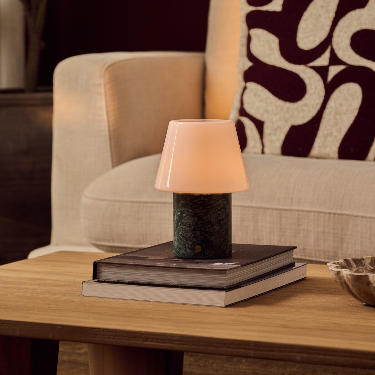 Hooch Green rechargeable table lamp with tapered glass shade and marble base resting on stacked books