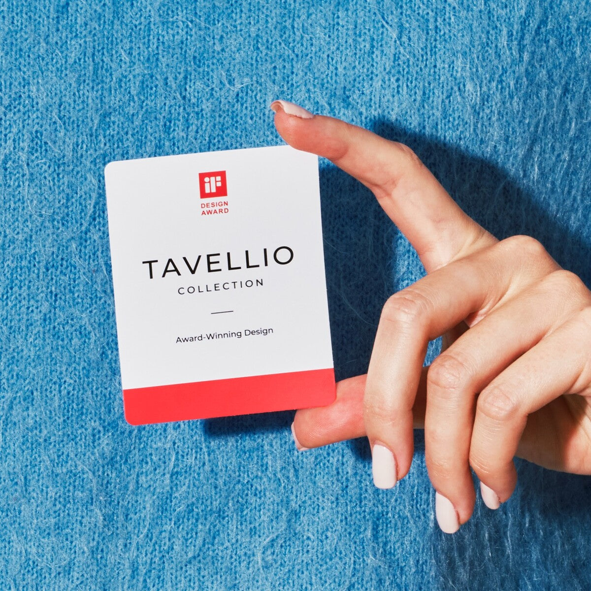 Hand holding the Tavellio iF Design Award card recognising the Rosa Aurora marble table lamp
