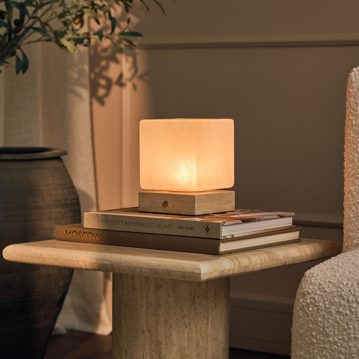 Tafellamp oplaadbaar Keyser op een ronde travertijnen bijzettafel naast boeken en een olijftak