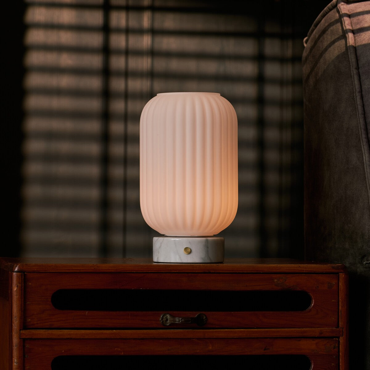 Tafellamp oplaadbaar Kota Bianco Statuarietto marmer, gloeiend naast jaloezieschaduw op een houten dressoir