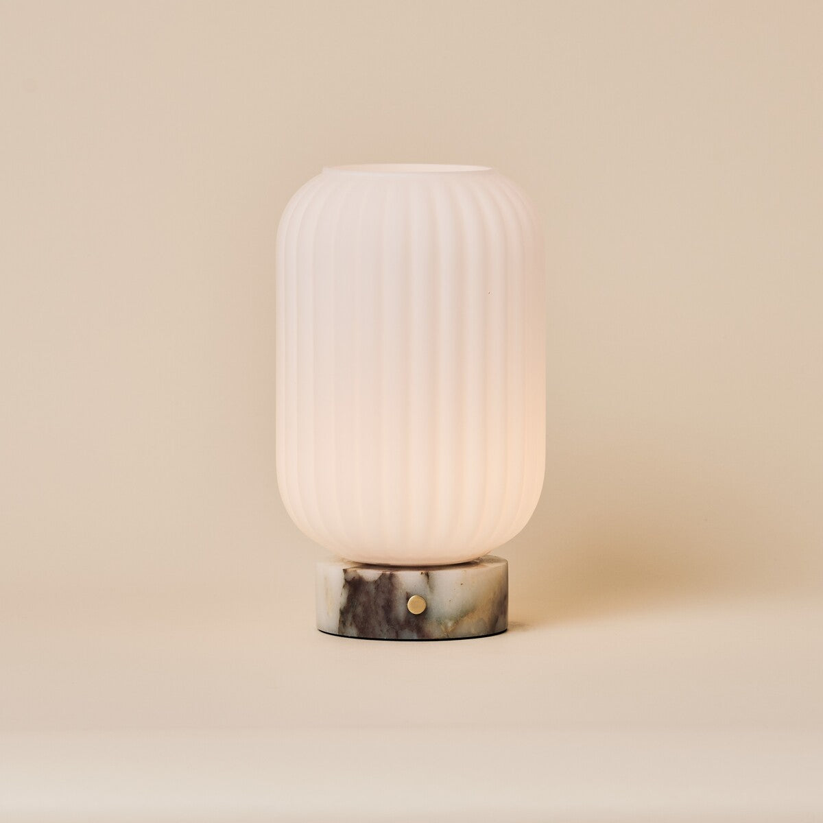 Oplaadbare tafellamp Kota met Calacatta Viola marmeren voet en geribbeld glazen kapje op een beige achtergrond
