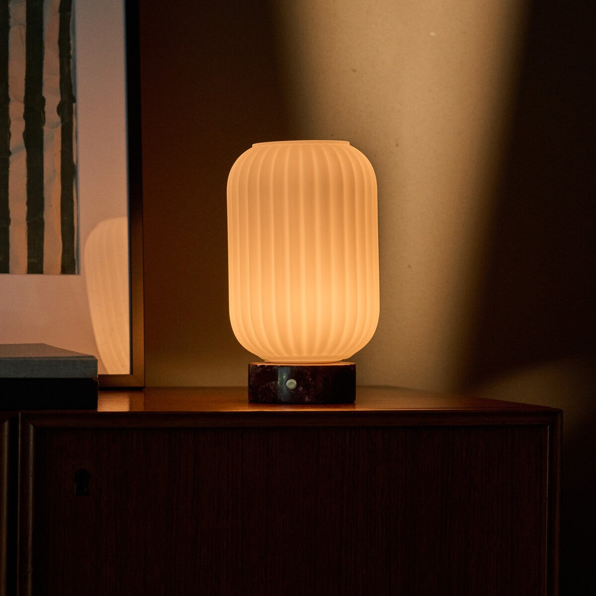Tafellamp oplaadbaar Kota Rosso Levanto marmer, zacht licht op een donker houten nachtkastje in de avond