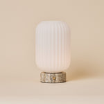 Oplaadbare tafellamp Kota met geribbelde glazen kap en Silver Travertine voet op een egale achtergrond