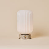 Oplaadbare tafellamp Kota met geribbelde glazen kap en Silver Travertine voet op een egale achtergrond