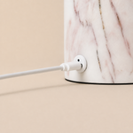 Gros plan sur le socle en marbre lilas pâle d'une lampe Tavellio – détail du connecteur de charge USB-C et de son câble blanc