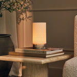 Oplaadbare tafellamp Luna verlicht op een stapel designboeken naast een olijfboom binnenshuis
