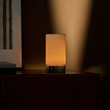 Oplaadbare tafellamp Luna werpt warm licht op een donker houten ladekast door gestreepte jaloezieschaduw