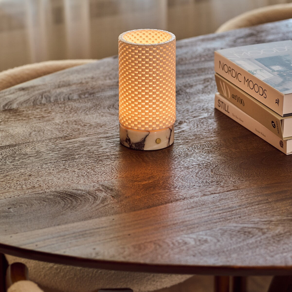 Tafellamp oplaadbaar Luna verlicht op een ronde houten tafel naast een stapel interieurboeken