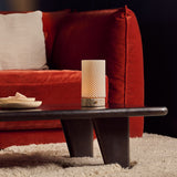 Oplaadbare tafellamp Luna in Silver Travertine en porselein op een zwarte salontafel naast een roestrode fluwelen bank.