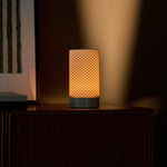 Tafellamp Luna oplaadbaar in Silver Travertine en porselein, gloeiend op een donker houten kast in de avond.