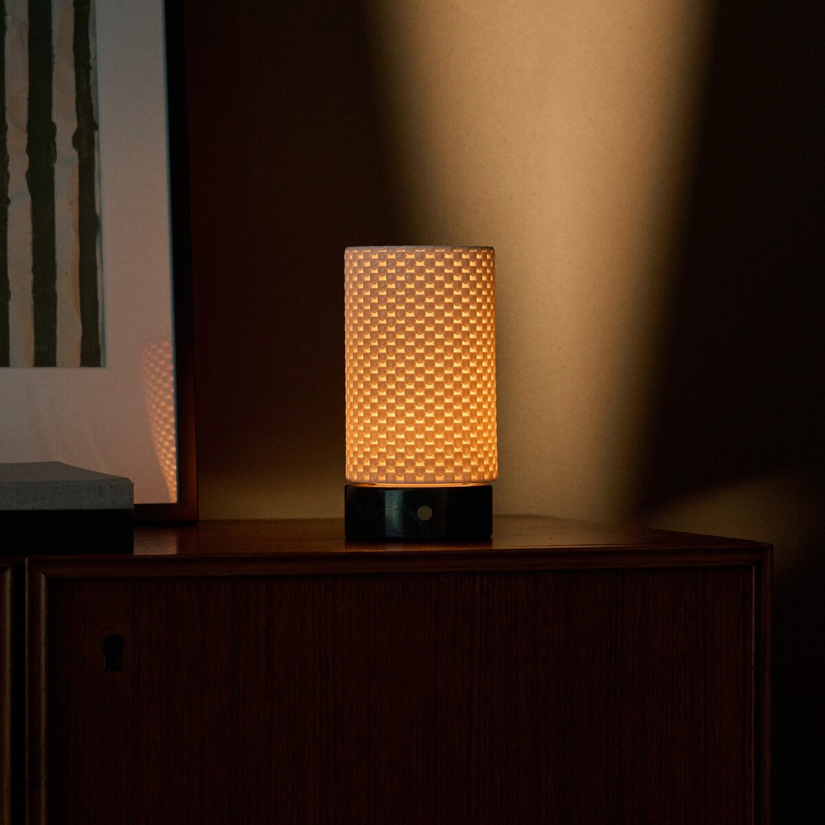 Tafellamp oplaadbaar Luna werpt warm licht over de wand boven een houten dressoir in de schemering