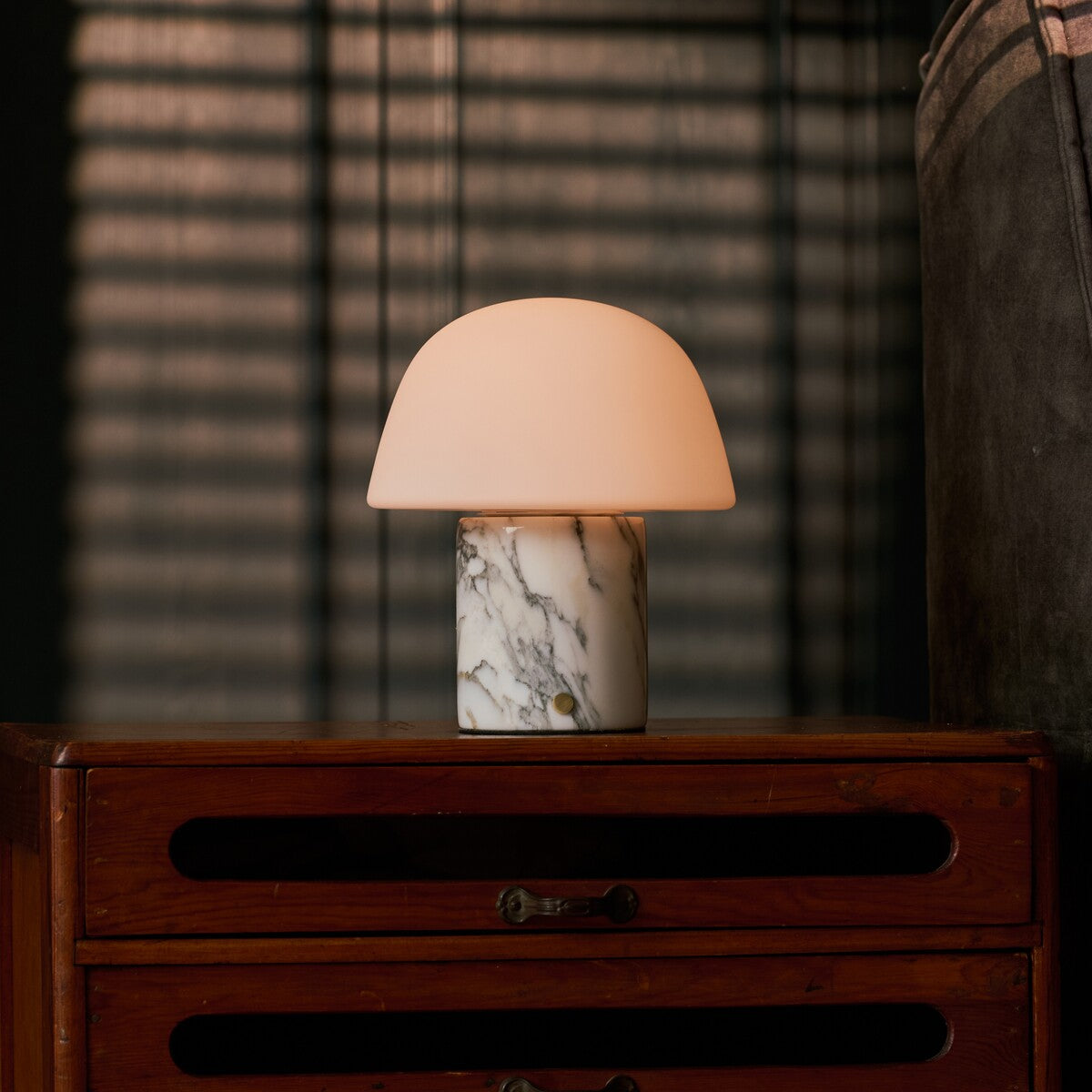 Oplaadbare tafellamp Maes Arabescato marmer warm licht verspreidend naast een groen gestreepte plant