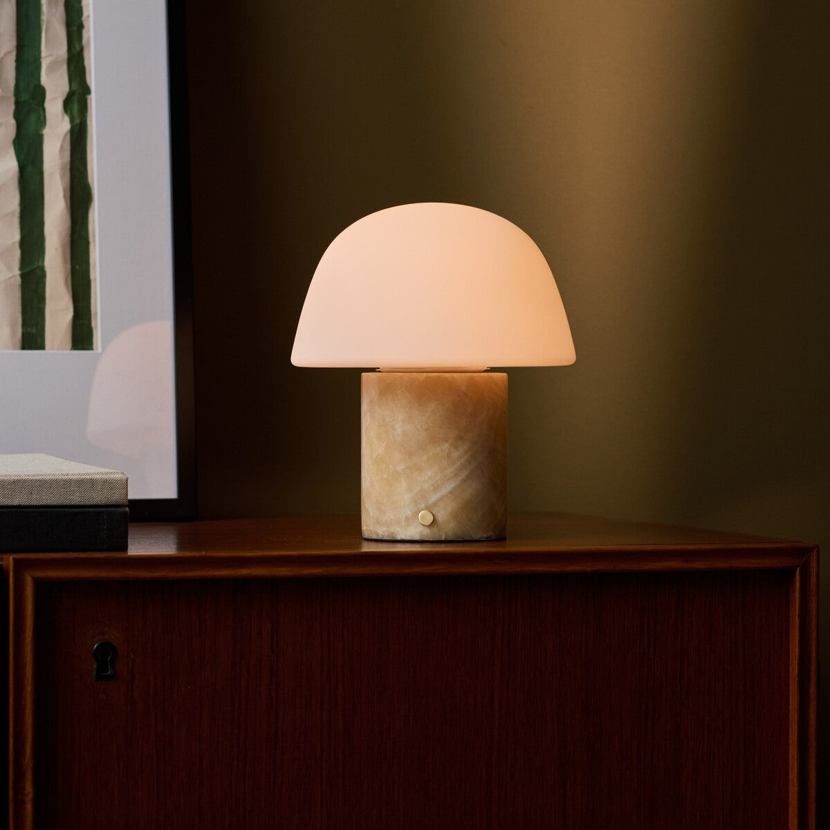 Oplaadbare tafellamp Maes Honey Onyx marmer verlicht op een walnoten dressoir naast een ingelijst kunstwerk