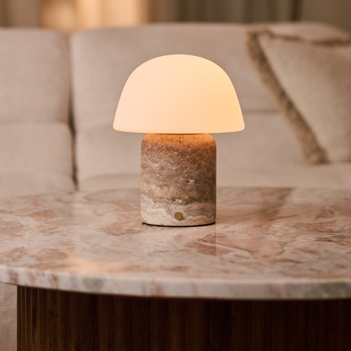 Tafellamp oplaadbaar Maes Large in silver travertine, gloeiend op een roze marmeren bijzettafel