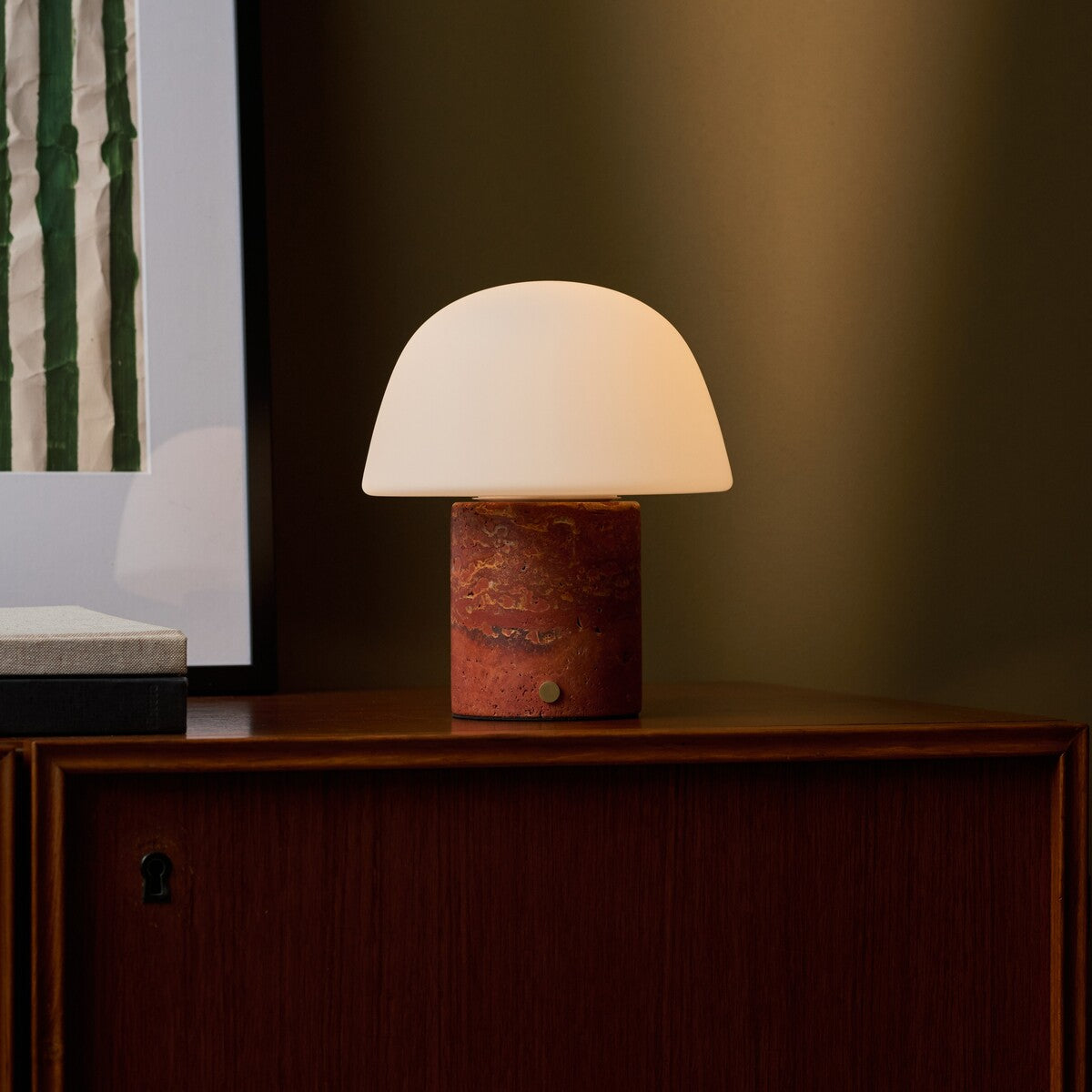 Oplaadbare tafellamp Maes Red Travertine verlicht op een houten dressoir tegen een olijfgroene wand