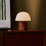 Oplaadbare tafellamp Maes Red Travertine verlicht op een houten dressoir tegen een olijfgroene wand