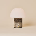 Oplaadbare tafellamp Maes Silver Travertine marmer met melkglazen bolkap op een neutrale studioachtergrond