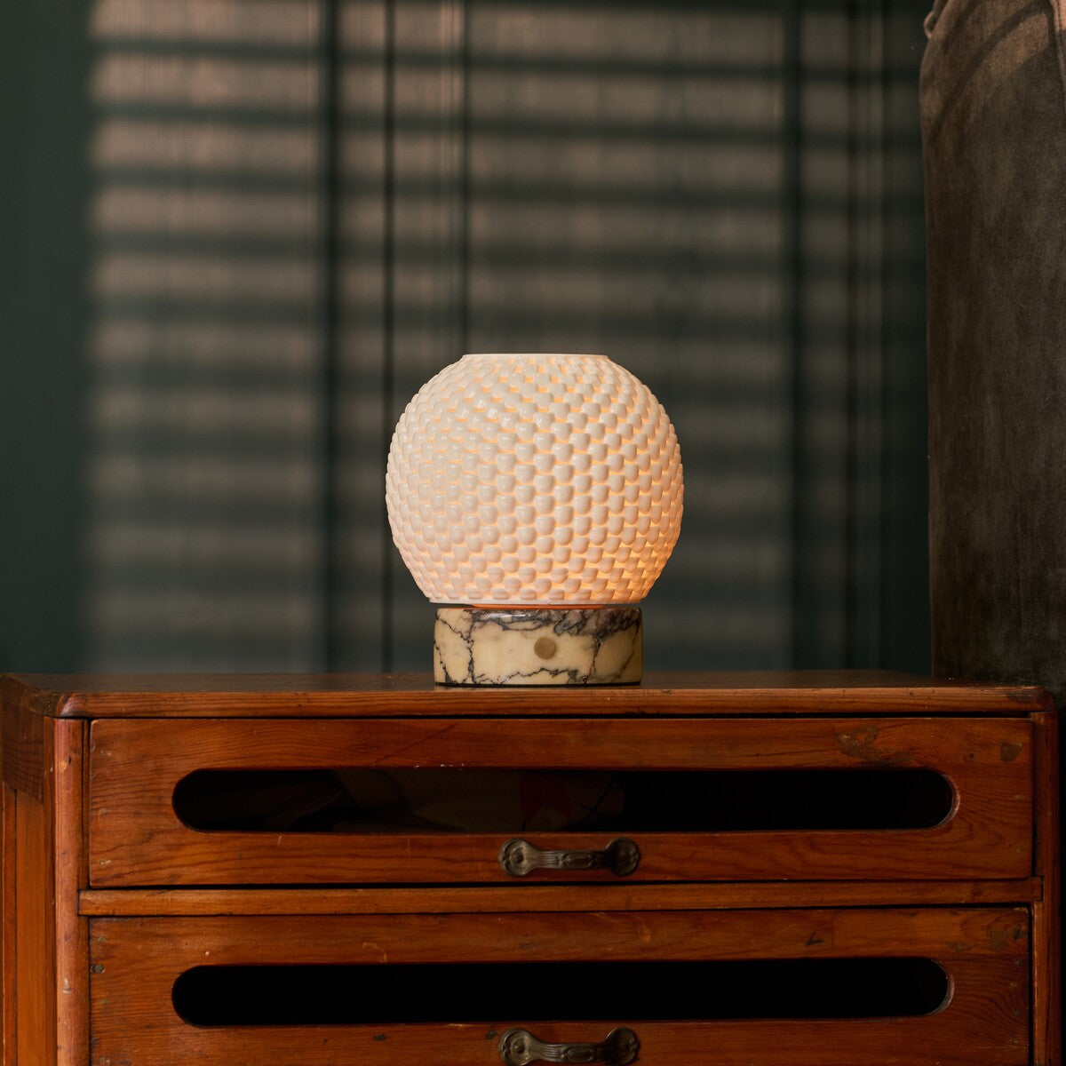 Mare cordless table lamp on a wooden nightstand in front of striped window blinds