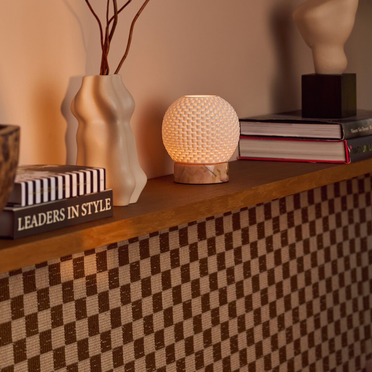Mare rechargeable table lamp with pink marble base styled on a shelf beside ceramic vases and books