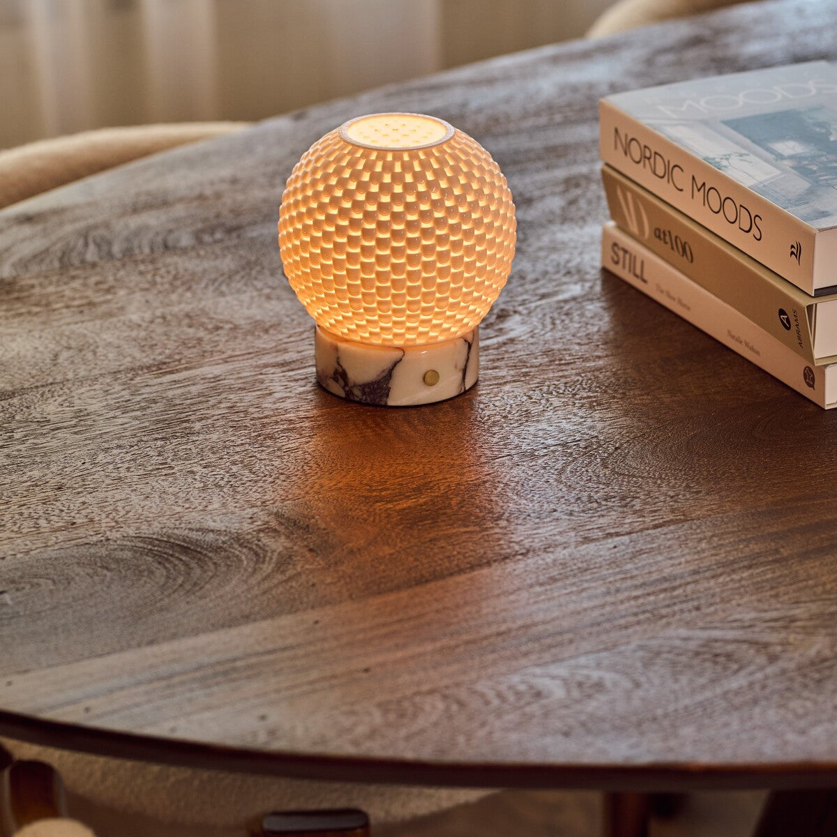 Oplaadbare tafellamp Mare met witte marmeren voet op ronde houten eettafel naast een stapel boeken
