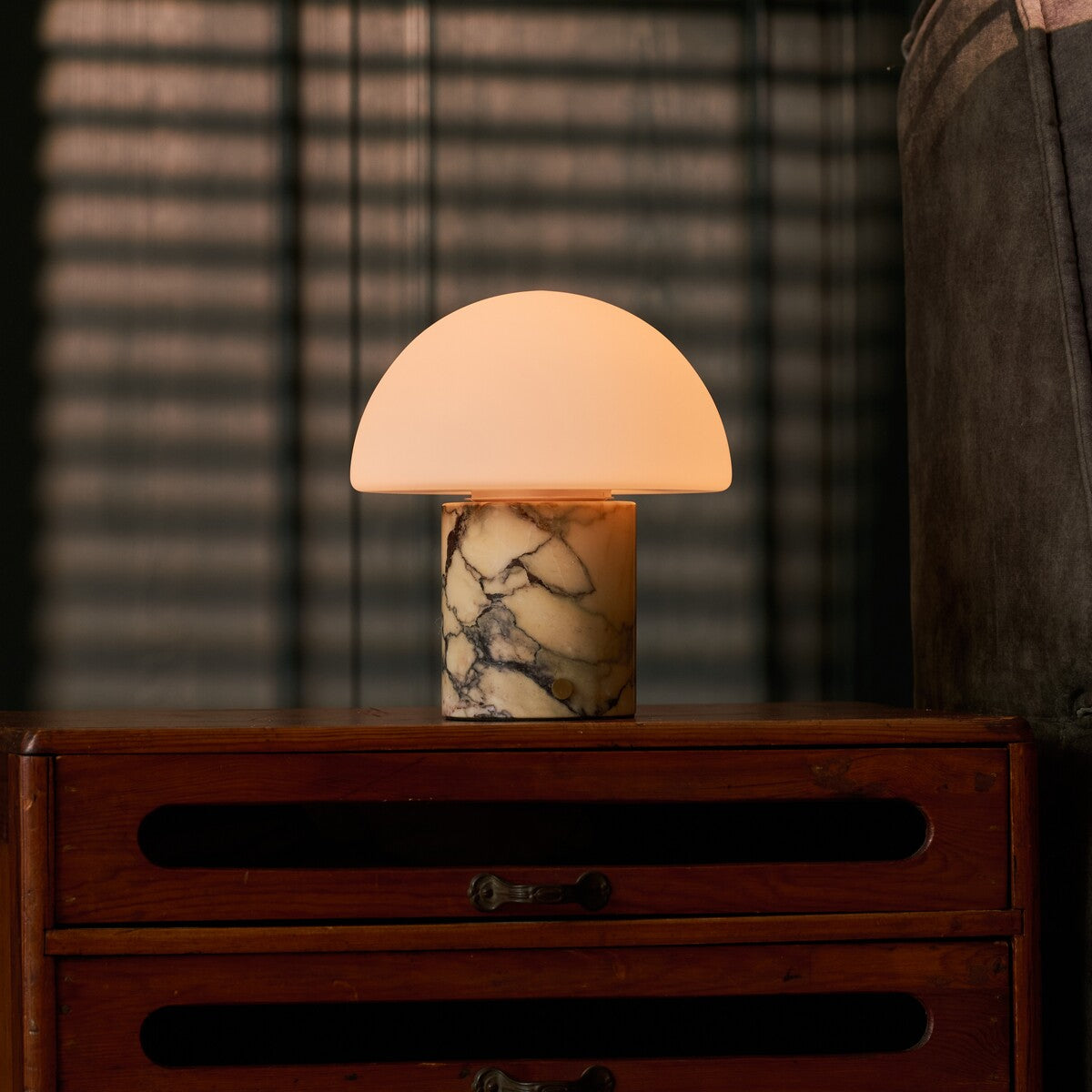 Mare rechargeable table lamp with gold-veined marble base beside a striped blind and chair