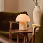 Oplaadbare tafellamp Maris in honingkleurig onyx marmer op bijzettafel naast groene fluwelen stoel