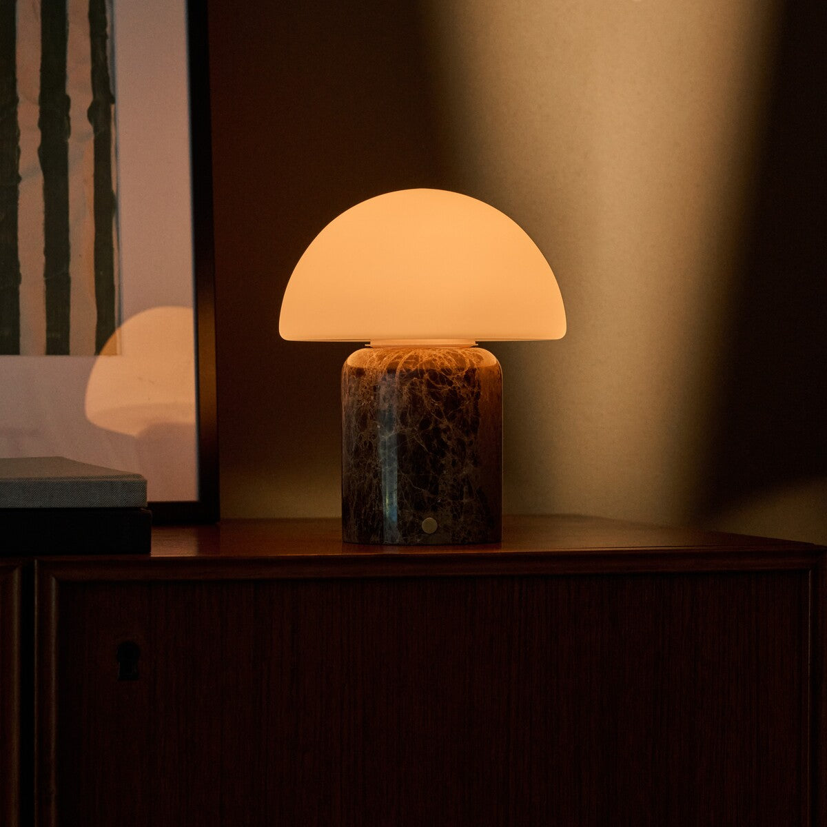 Oplaadbare tafellamp Maris Large gloeit bij schemering op een donker houten dressoir