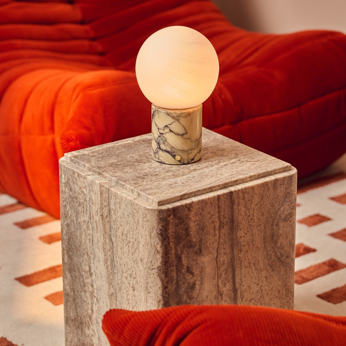 Rechargeable table lamp in Calacatta Vionaro marble on a travertine side table beside an orange velvet sofa