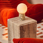 Rechargeable table lamp in Calacatta Vionaro marble on a travertine side table beside an orange velvet sofa