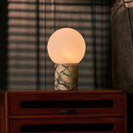 Rechargeable table lamp in Calacatta Vionaro marble on a wooden nightstand beside striped blinds