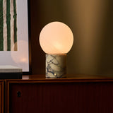 Rechargeable table lamp in Calacatta Vionaro marble glowing on a wood sideboard beside framed art