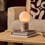 Oplaadbare tafellamp Metsu Large Silver Travertine marmer op stapel boeken bij beige fauteuil